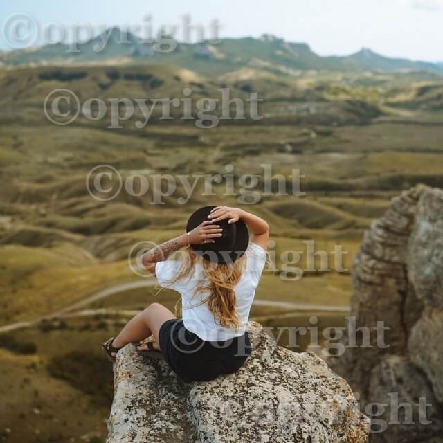 This example protects a JPG image of a girl sitting on the rocks from unauthorized copying. It adds a diagonal wall of "©opyright" watermarks to the image. The watermark is made 75% transparent, the text letters are white, and there's a black text shadow. Text size is 60px, line-height is 110px, and the font is George bold. (Source: Pexels.)